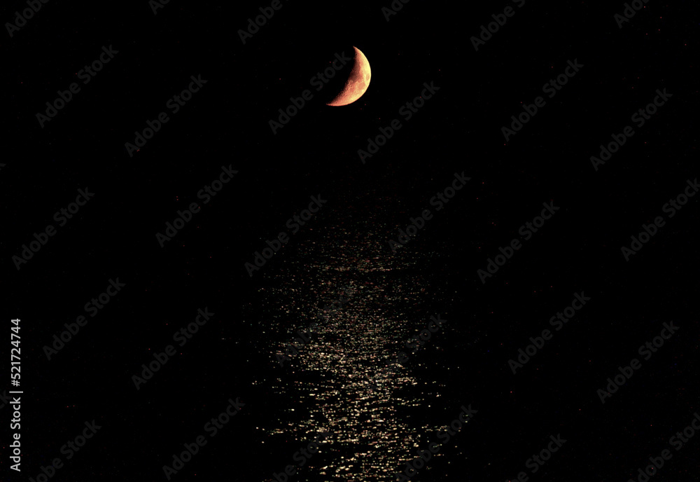 Fototapeta premium The new moon in the black night above the shiny surface of the sea
