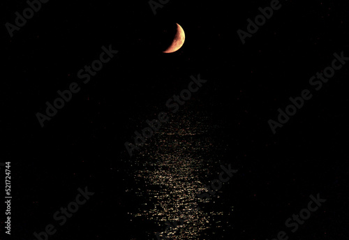 The new moon in the black night above the shiny surface of the sea