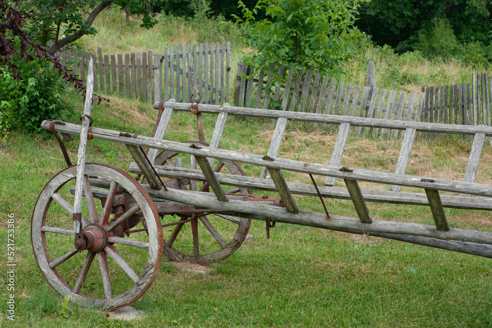 Old primitive wagon or cart sits in yard near a broken down fence in Serbia.  The weathered wagon shows a hand brake.