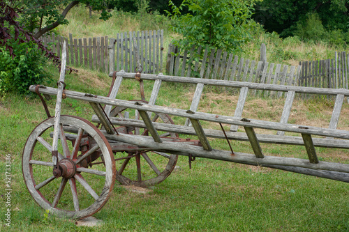 Old primitive wagon or cart sits in yard near a broken down fence in Serbia. The weathered wagon shows a hand brake.