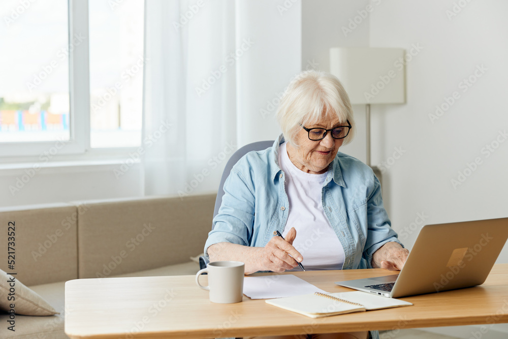 an attentive, responsible woman with gray hair, a pensioner, works from home at a laptop, carefully peering at the information on the monitor an attentive, responsible woman with gray hair, a pensioner, works from home at a laptop, carefully peering at the information on the monitor