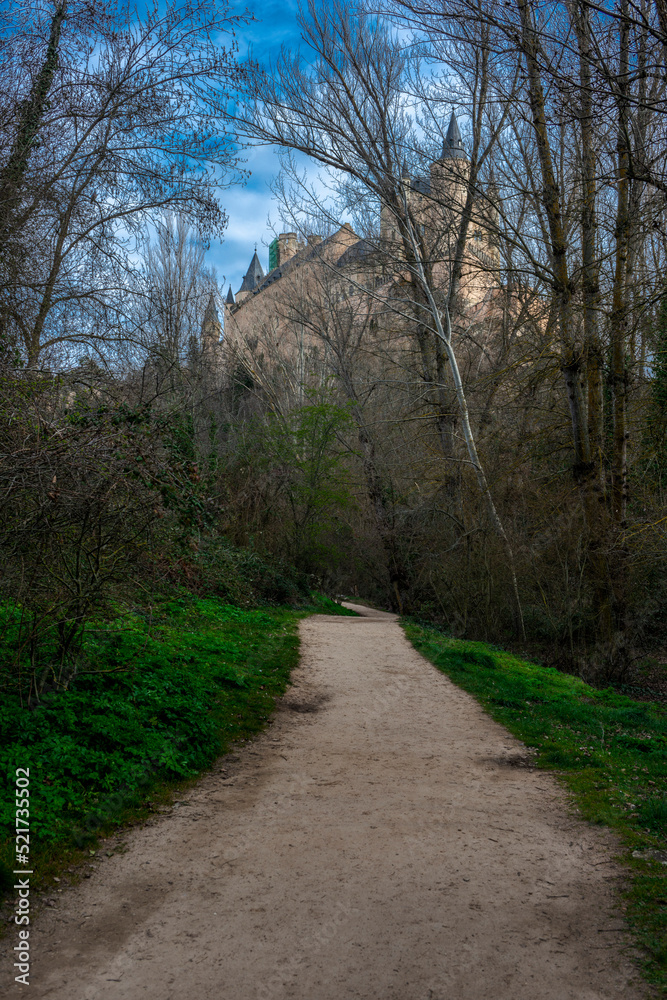 dirt road between trees and grass in the direction of the Alcazar of Segovia on a winter day with beautiful clouds and green grass on the ground dirt road between trees and grass in the direction of the Alcazar of Segovia on a winter day with beautiful clouds and green grass on the ground