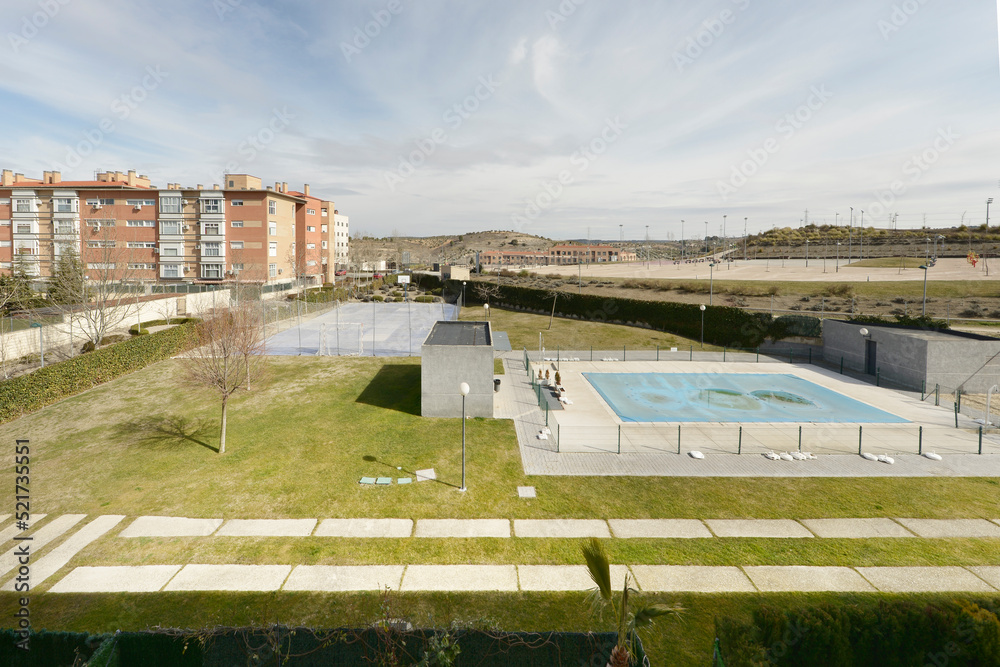 Obraz premium Views of an enclosed swimming pool and sports court and some residential developments on the outskirts of a city with gardens and stone paths