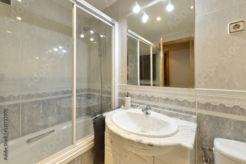 Bathroom with gray tiled walls and transparent sliding doors and frameless mirror on the wall