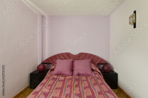 Awful furnished bedroom with upholstered headboard and light reddish colored cushions and duvet