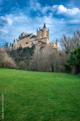 View of the Alcazar of Segovia on a winter day with beautiful clouds and green grass on the ground