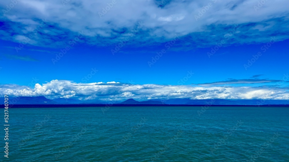 unrealistically white-gray silver Clouds on a bright blue sky a little Turquoise colorless water of the Pacific Ocean divide picture into two parts background for any title text or advertising travel