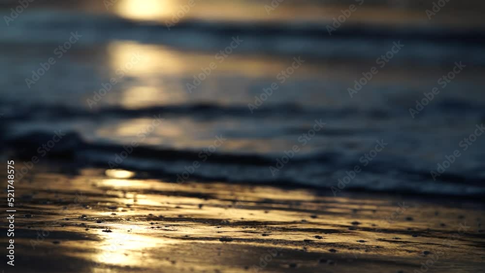 sunrise reflecting on the beach with golden light as waves roll in and water moves on the sand, calming waves