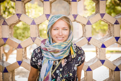 A blonde model dressed appropriately standing and smiling in front of a Central Asian wall. photo