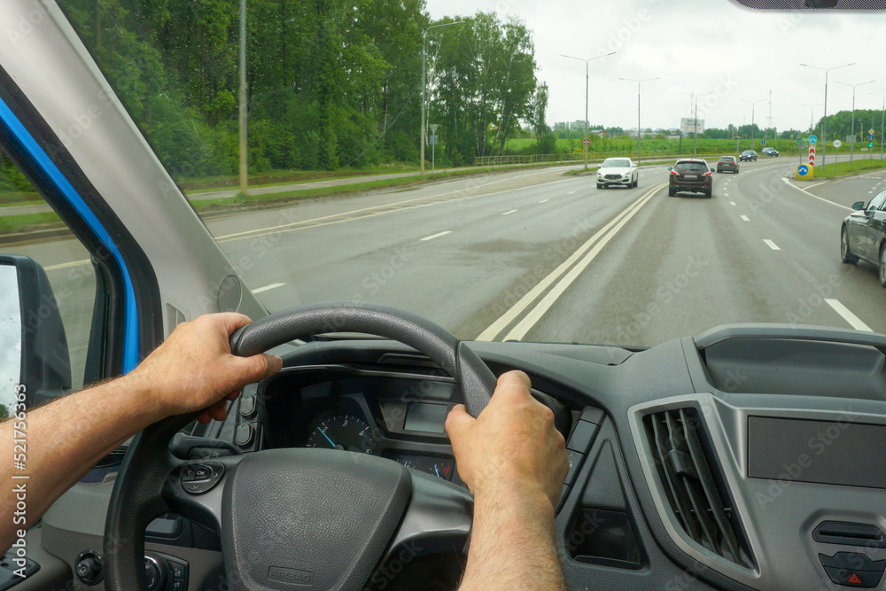  Руки водителя на рулевом колесе автомобиля во время движения по шоссе. Вид из кабины автомобиля.