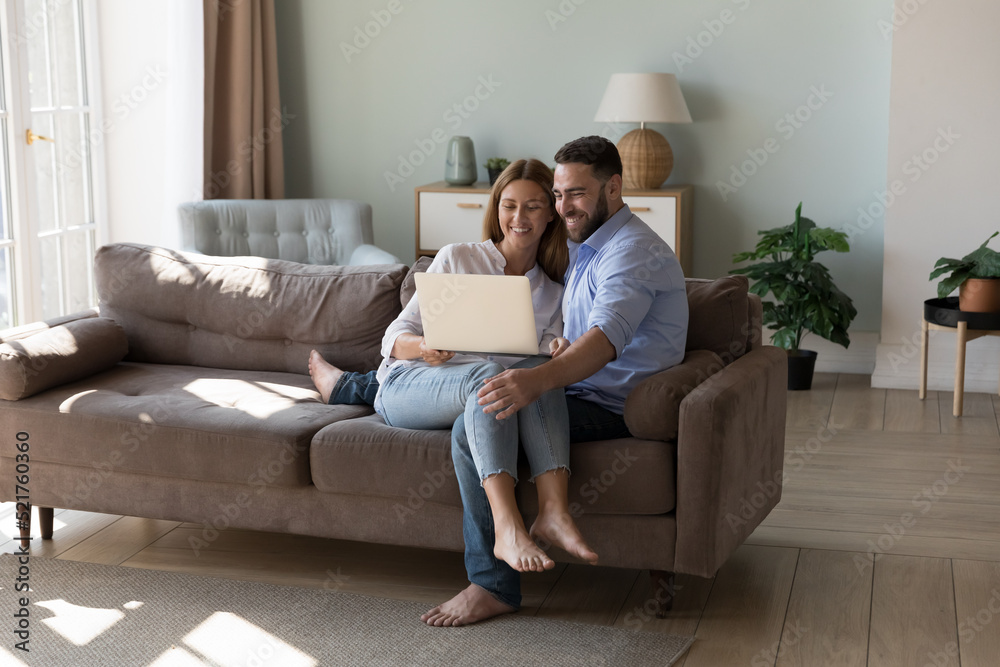 Couple sit on sofa use laptop make on-line purchase, order services, buy goods, search home decorations ideas on internet spend time with modern technology. E-commerce clients for comfort life concept Couple sit on sofa use laptop make on-line purchase, order services, buy goods, search home decorations ideas on internet spend time with modern technology. E-commerce clients for comfort life concept