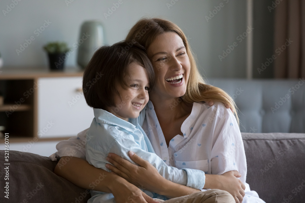 Happy young woman cuddles her preschooler 6s son. Loving mother spend time with cute cheery little child sit on sofa look overjoyed, enjoy leisure at home feeling attachment, love. Motherhood concept Happy young woman cuddles her preschooler 6s son. Loving mother spend time with cute cheery little child sit on sofa look overjoyed, enjoy leisure at home feeling attachment, love. Motherhood concept