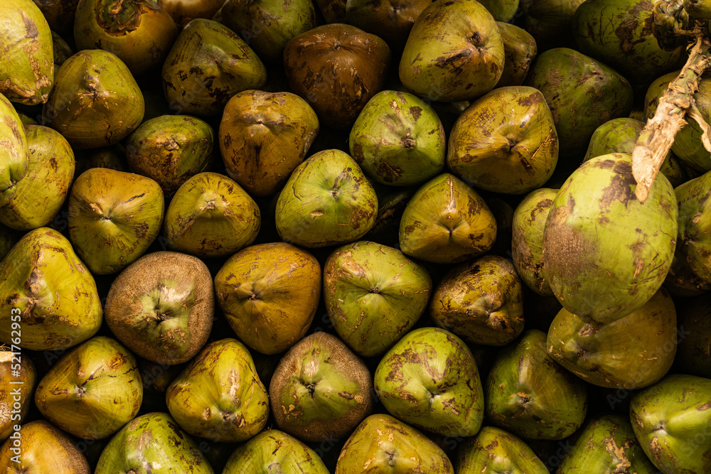 Green coconut fruits, piled on a stall at the bazaar, natrual food background or texture.