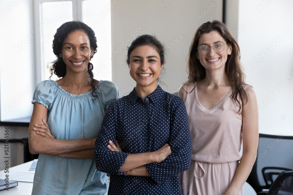 Three multi ethnic businesswomen staff members with cross-armed pose at workplace smile look at camera. Group of friendly company female employees, quality services, career growth, partnership concept Three multi ethnic businesswomen staff members with cross-armed pose at workplace smile look at camera. Group of friendly company female employees, quality services, career growth, partnership concept