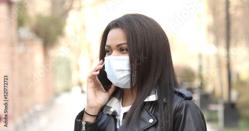 Health, safety and pandemic concept. Young woman wearing black face protective reusable barrier mask outdoors calling on smartphone. © lashkhidzetim