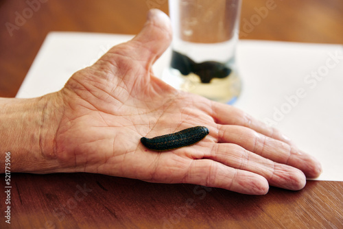 Man puts hand on wooden table near glass showing black leech photo