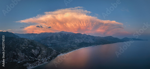 Panoramic coastal landscape, evening aerial view of the Albanian Riviera against a dramatic sky. Beach, mountains, pink illuminated storm cloud. Summer. Borsh, Albanian Riviera. Travelling Albania.