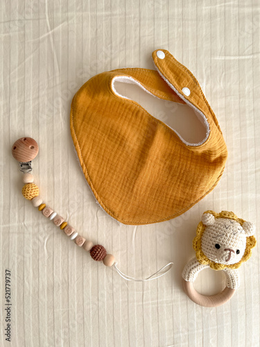 Foto Composition with baby muslin bibs, rattles with a knitted bodice and chains of wooden beads with a nipple clothespin on a light background