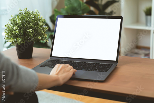 Woman hand using laptop and typing on keyboard with mockup of blank screen on wooden table.