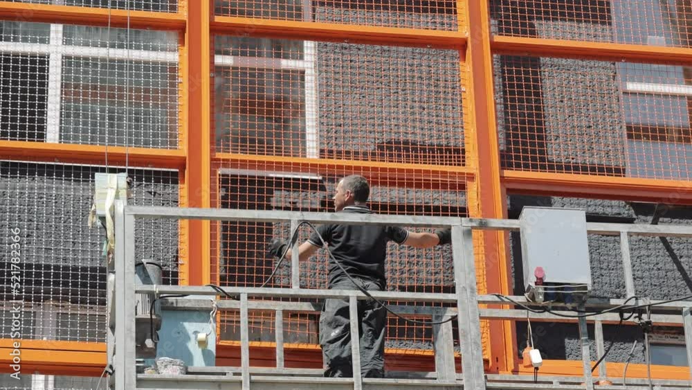 A builder on a lift installs a protective metal mesh on the facade of the house. Decoration of the facade of the house. A builder on a lift installs a protective metal mesh on the facade of the house. Decoration of the facade of the house.