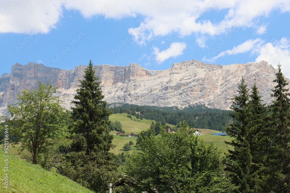 Obraz premium Coravara, Italy-July 16, 2022: The italian Dolomites behind the small village of Corvara in summer days with beaitiful blue sky in the background. Green nature in the middle of the rocks.
