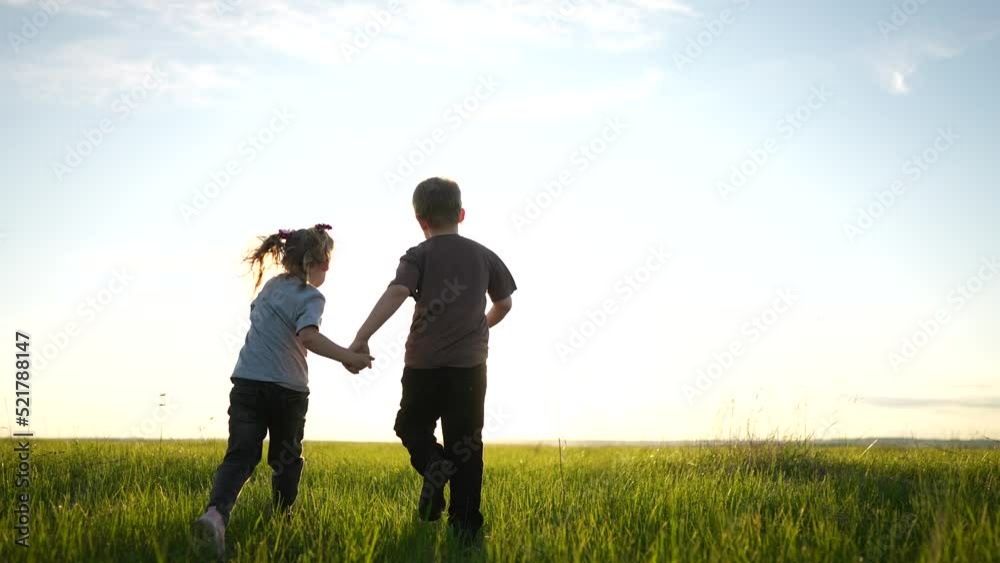 boy girl a running in the park. happy family kid dream holiday concept. children hold hands brother sister run across the field silhouette summer in sun the park. kids run boy girl a running in the park. happy family kid dream holiday concept. children hold hands brother sister run across the field silhouette summer in sun the park. kids run