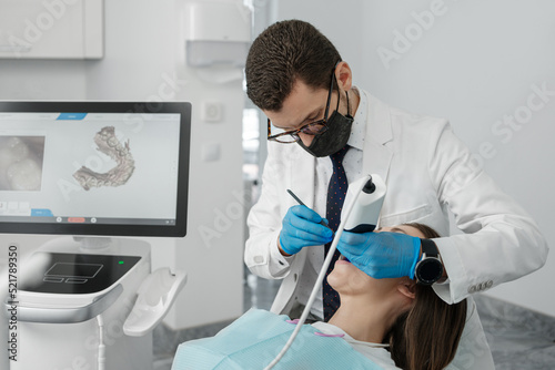 Male orthodontist scaning patient with dental intraoral scanner and controls process on screen. photo