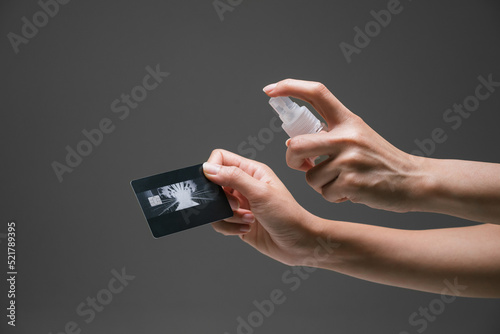 Lady hand applying alcohol spray hand sanitizer towards the credit card to prevent the spread of bacteria and virus. Personal hygiene concept. Isolated black background