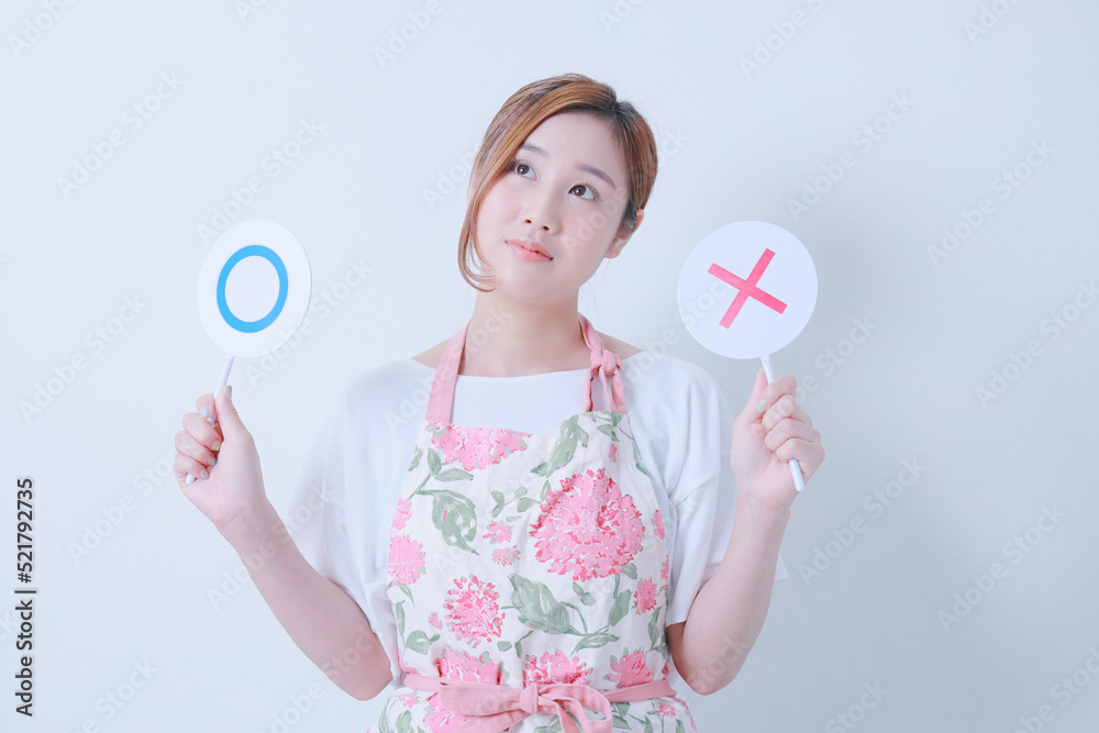 ○✖️の札を持つエプロン姿の若い女性 ○✖️の札を持つエプロン姿の若い女性