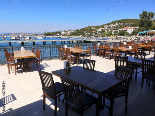 Holztische und Stühle auf der Terrasse und Veranda eines Restaurant mit Panoramablick im Sommer bei blauem Himmel und Sonnenschein in Ayvalik in der Provinz Balikesir am Ägäischen Meer in der Türkei photo