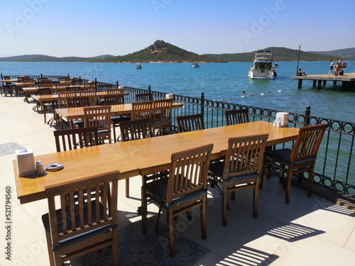 Holztisch mit Stühlen auf der Terrasse eines Restaurant mit Panoramablick im Sommer bei blauem Himmel und Sonnenschein am Strand von Ayvalik in der Provinz Balikesir am Ägäischen Meer in der Türkei photo