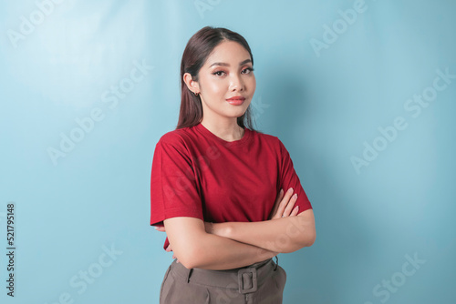 Portrait of a confident smiling girl standing with arms folded and looking at the camera isolated over blue background, wearing a red t-shirt