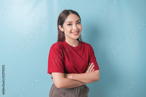 Portrait of a confident smiling girl standing with arms folded and looking at the camera isolated over blue background, wearing a red t-shirt
