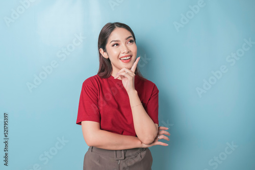 Portrait of a thoughtful young casual girl wearing a red t-shirt looking aside isolated over blue background