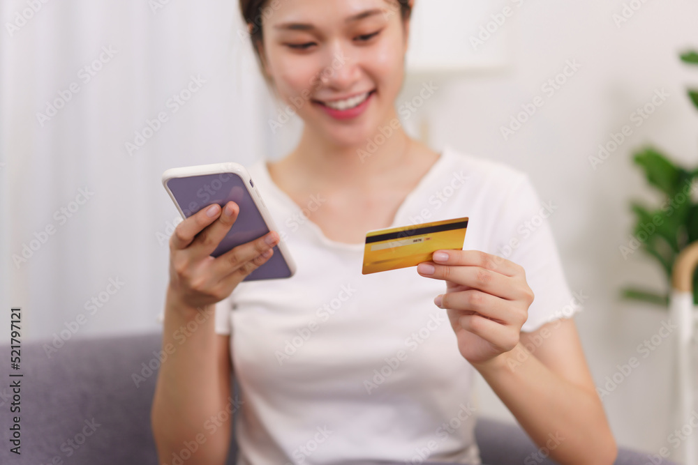 Lifestyle in living room concept, Asian woman holding credit card and use phone to online shopping Lifestyle in living room concept, Asian woman holding credit card and use phone to online shopping