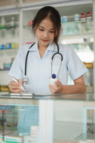 Medicine and health concept, Female pharmacist hold pill bottle and write prescription in pharmacy