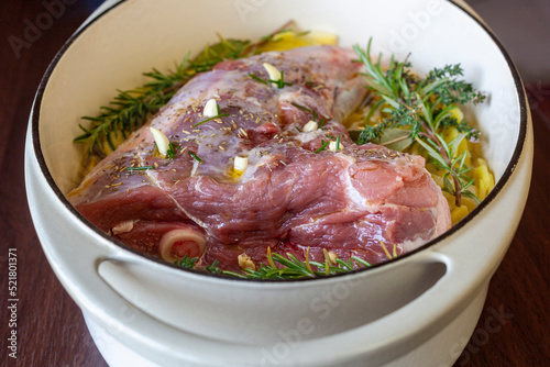 Raw leg of lamb prepared to cook with sliced potatoes and provencal herbs
