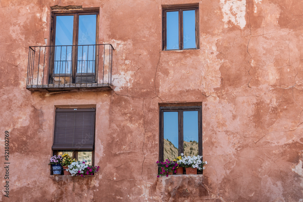 Windows and balconies adorned with plants, on a brown stucco wall.