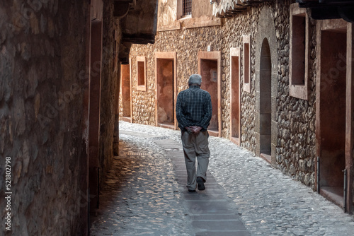 Man from behind walks calmly through the streets of Albarracín.
