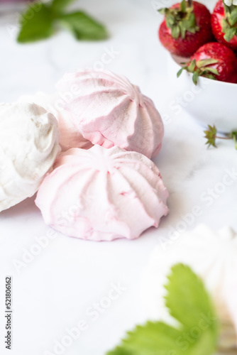 Red and white marshmallows on a white background next to a bowl of strawberries