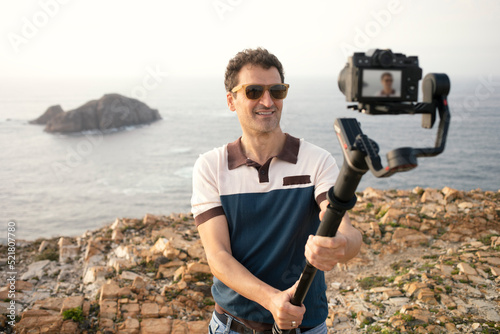 vlogger create digital content for vlog recording with camera on top gimbal stabilizer in beautiful landscape looking at camera.Using the gimbal camera stabilizer for professional content production