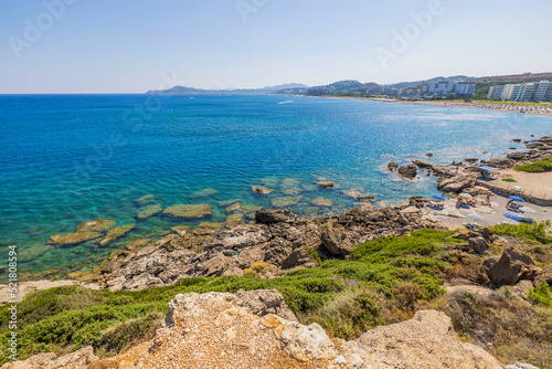 Beautiful view of rocky coast against background of turquoise water and coastline of hotels with sandy beaches. Greece.