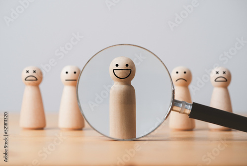 Smile face of wooden figure inside of magnifier glass among sad face for customer focus and relation management , excellent evaluation after client use product and service concept.