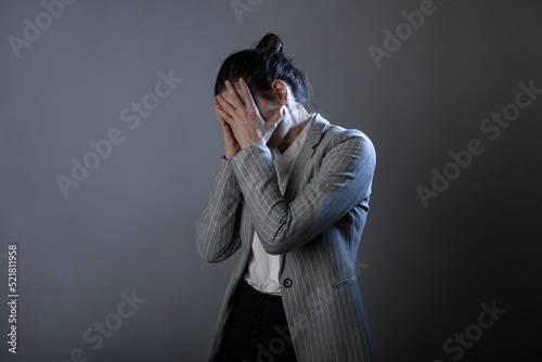 Blood pressure, migraine or headache, a young woman in a business suit standing clutching head, portrait on a gray background