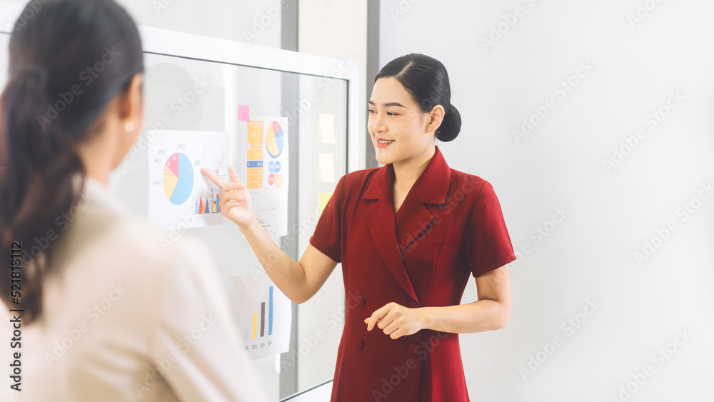Fototapeta premium Busy young adult business asian woman expand analysis finance graph on glass board at indoor office