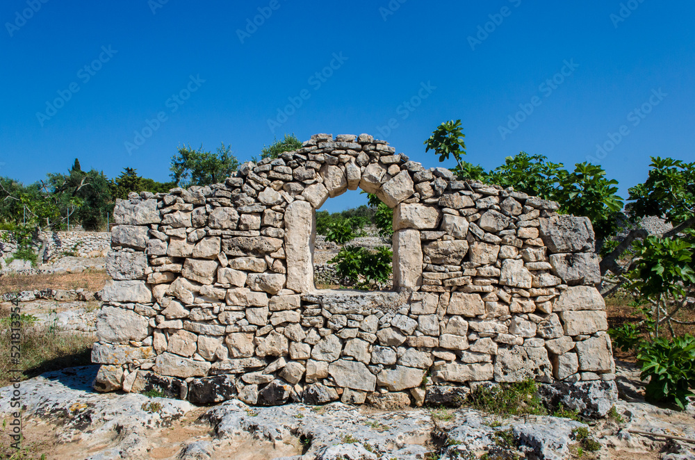 La facciata di un vecchio edificio con una finestra ad arco realizzato con muro a secco nella campagna del Salento in Puglia con gli ulivi secolari che crescono in un campo dalla tipica terra rossa La facciata di un vecchio edificio con una finestra ad arco realizzato con muro a secco nella campagna del Salento in Puglia con gli ulivi secolari che crescono in un campo dalla tipica terra rossa