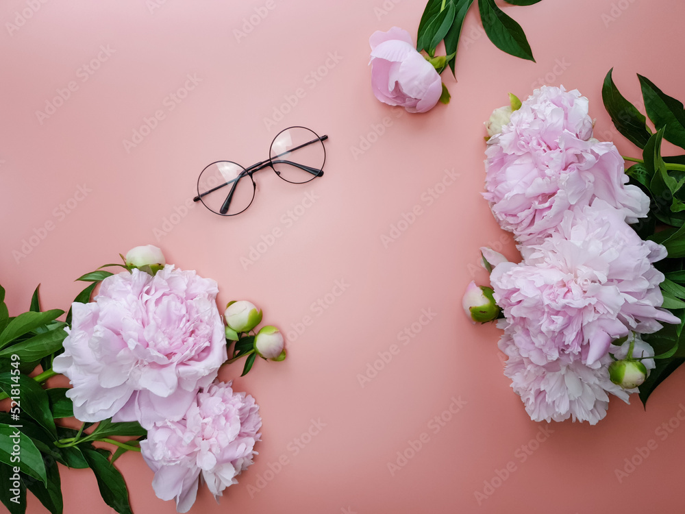 On a pink background lies a pair of glasses and pink peonies