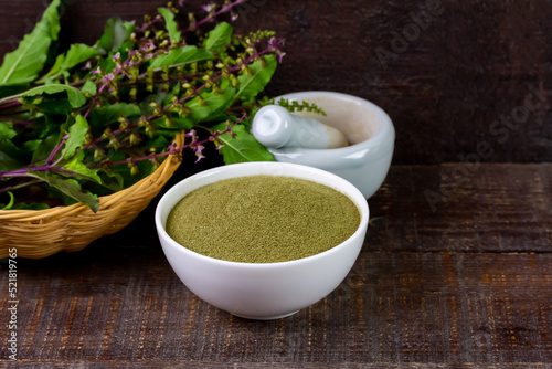 Holy basil powder on white bowl with branch and white mortar and pestle on rustic wooden background. Holy basil leaf are useful herbs and food ingredient has a spicy flavor. 