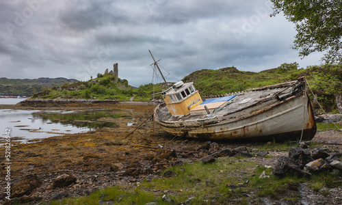 Ein altes Schiffswrack und dahinter die Ruinen einer Burg aus dem 15. Jahrhundert  - fotografiert auf der Isle of Skye in Schottland
