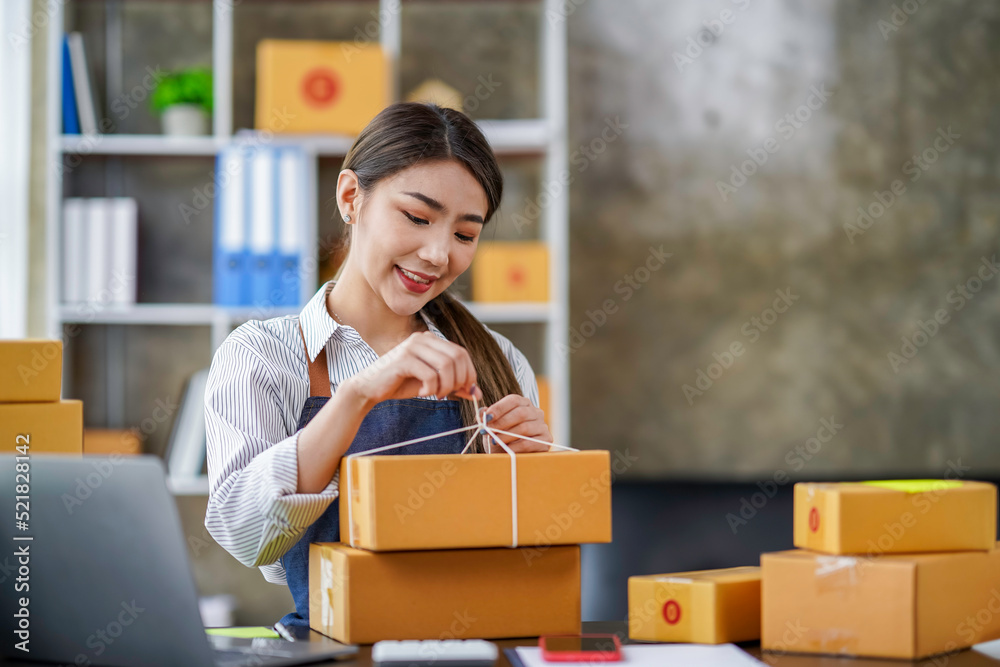 Asian businesswomen tie boxes with ropes in preparation for delivery to customers. Young Asian small business owners use computers. Shipping boxes online market SME e-commerce telemarketing concept Asian businesswomen tie boxes with ropes in preparation for delivery to customers. Young Asian small business owners use computers. Shipping boxes online market SME e-commerce telemarketing concept